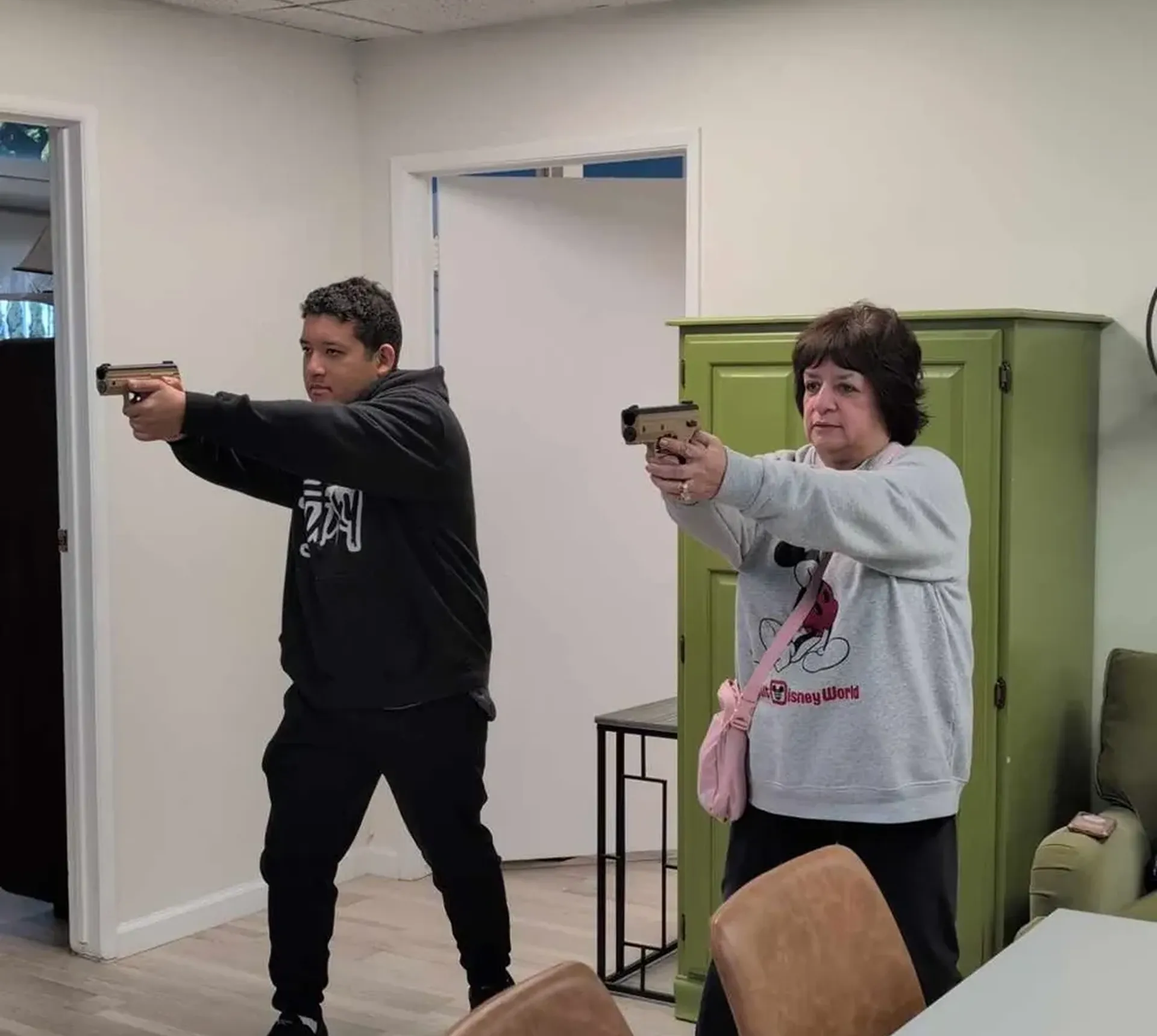 Two people aiming guns in a room.